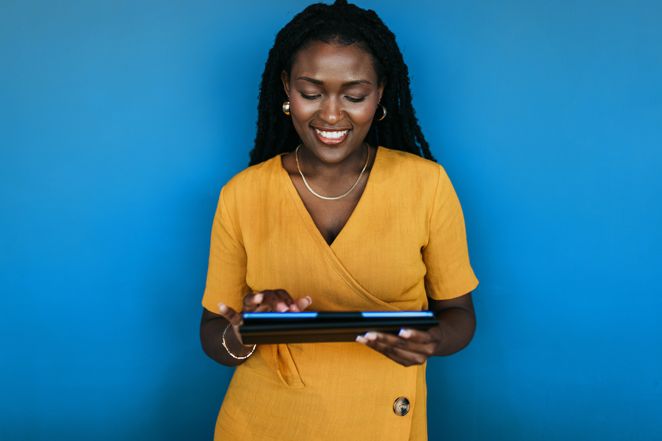 Portrait of young woman smiling cheerfully at digital tablet against blue background
